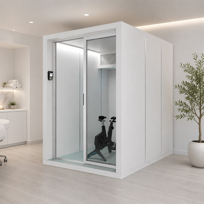 Altitude Centre MetraFit 3000 POD in white with aluminium-framed sliding glass doors, exercise bike inside, installed in a spa treatment room with marble counter and treatment bed.