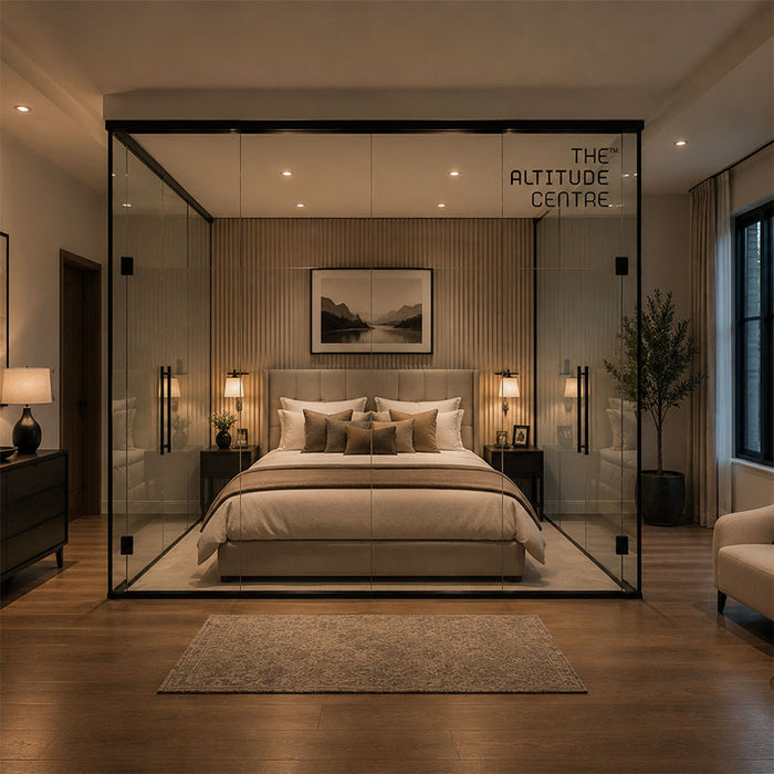 Altitude Centre MetraFit Sleep glass enclosure with black frame surrounding a double bed with warm beige and tan bedding, installed in a neutral-toned bedroom with wood flooring and fluted wall panelling.