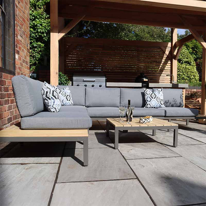 Aspen 6 Seater Corner Lounge Set from Teak Wood in a contemporary garden, showcasing spacious seating with grey cushions and a matching coffee table.