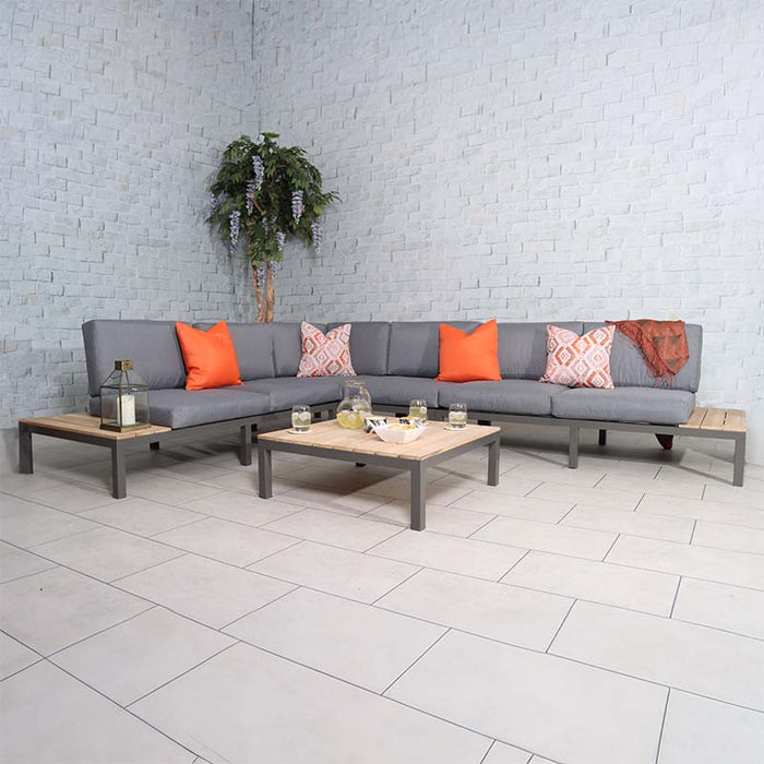 Aspen 6 Seater Corner Lounge Set with teak wood and grey cushions, adorned with orange accent pillows for a vibrant indoor setup.