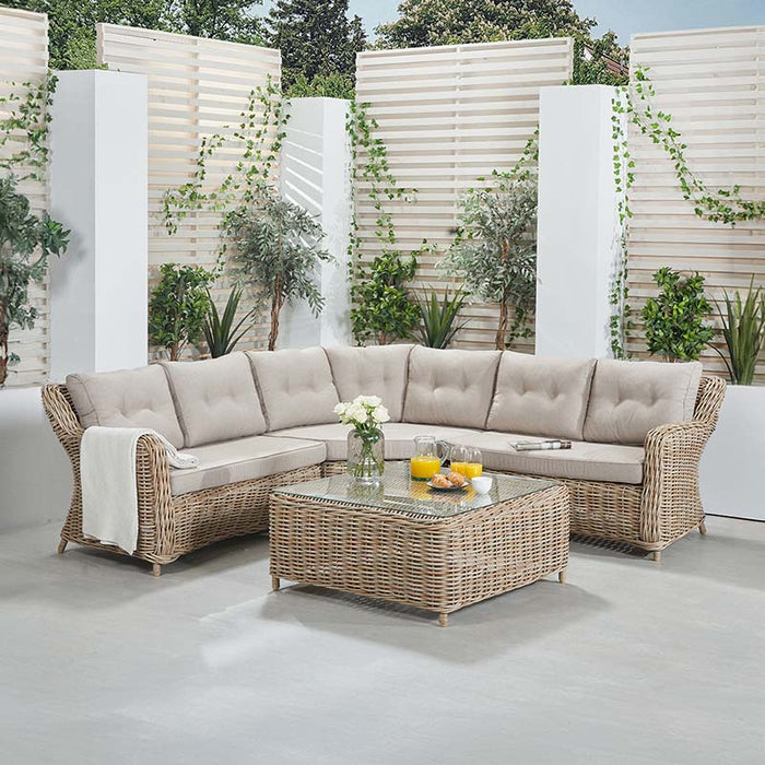 Barakaldo Natural Antique Outdoor Corner Set with beige cushions, displayed in a beautifully decorated patio setting, showcasing its inviting design.