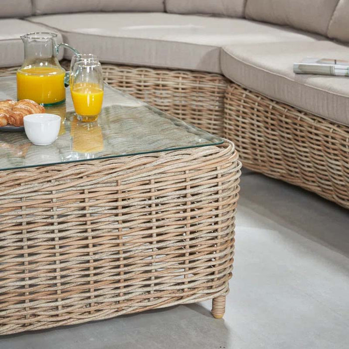 Detailed view of the tempered glass top and rattan weave of the coffee table from the Barakaldo Natural Antique Outdoor Corner Seating Set.