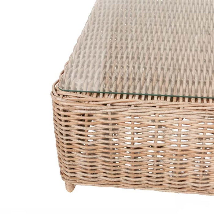 Close-up view of the left corner of the rattan coffee table with a glass top, part of the Barakaldo Natural Antique Outdoor Corner Seating Set.