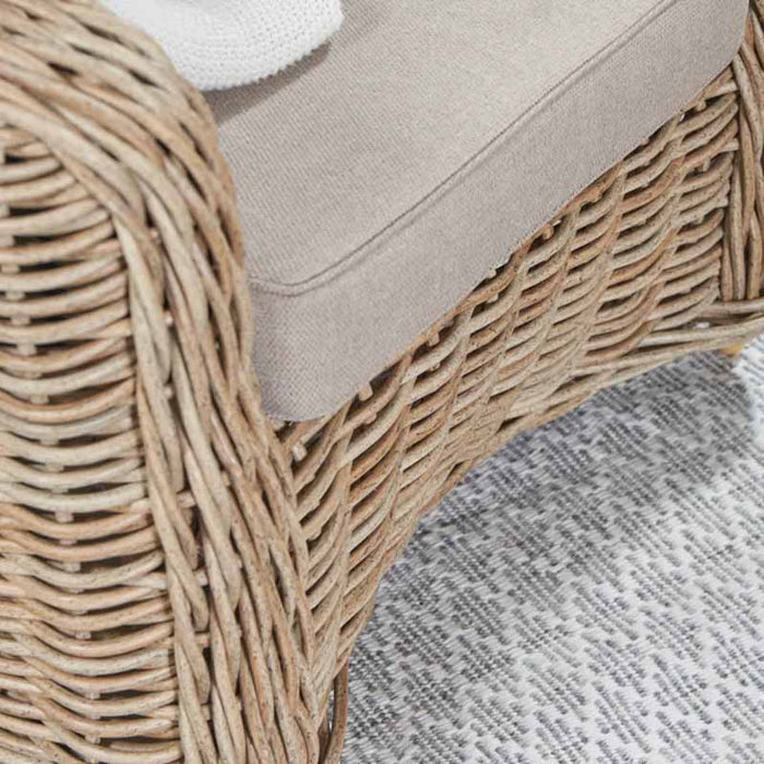 Close-up of the Barakaldo Natural Antique Outdoor Seating Set's armchair base, focusing on the detailed rattan weave and the beige cushion.