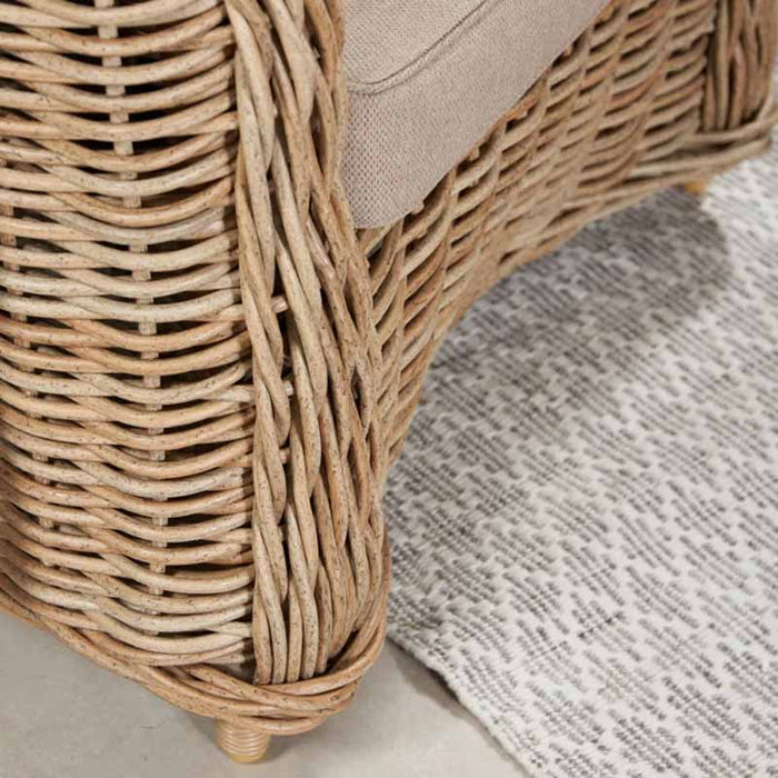 Detailed view of the Barakaldo Natural Antique Outdoor Seating Set's armchair legs, highlighting the sturdy rattan weave and elevated design.