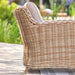 Side view of the Barakaldo Natural Antique Outdoor Seating Set's armchair, showcasing the elegant rattan weave and plush beige cushion in an outdoor setting.