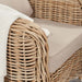 Detailed view of the Barakaldo Natural Antique Outdoor Seating Set's armrest with a beige cushion and a white blanket draped over it, highlighting the rattan craftsmanship.