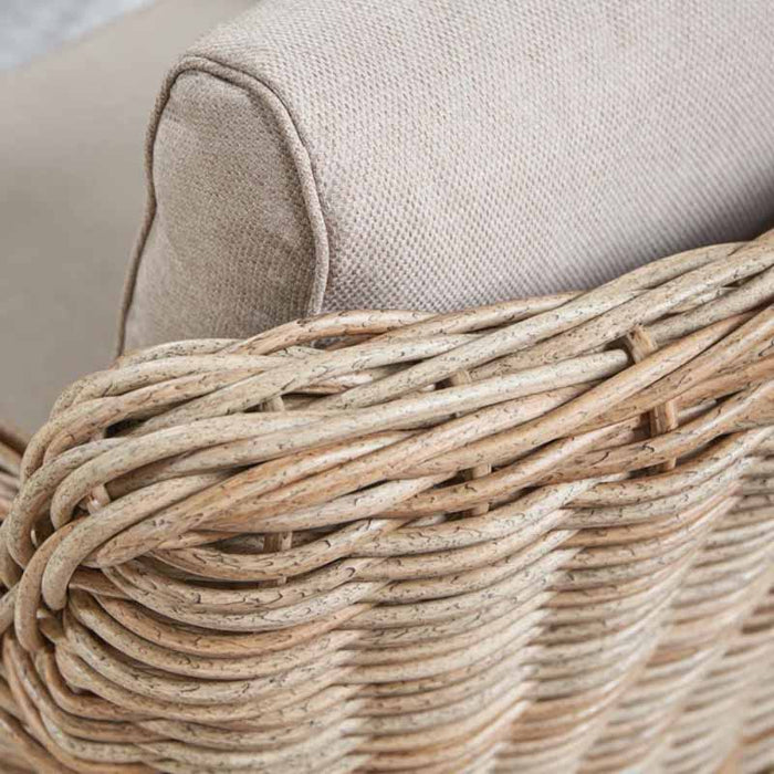 Close-up of the Barakaldo Natural Antique Outdoor Seating Set's armrest, showcasing the intricate rattan weave and the plush beige cushion.