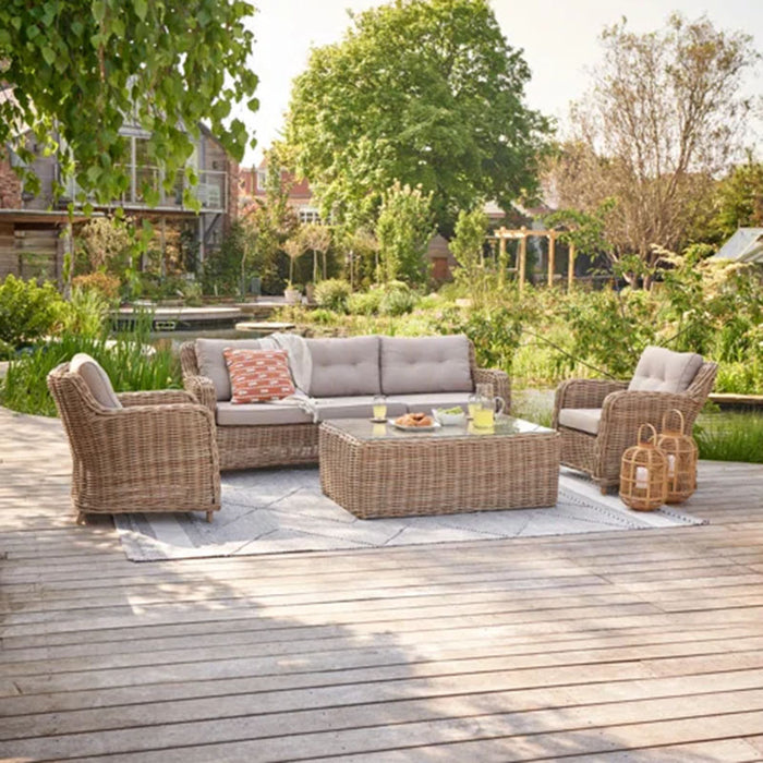 Barakaldo Natural Antique Outdoor Seating Set arranged in a garden setting, featuring a rattan sofa, armchairs, and a coffee table, providing a stylish outdoor living space.