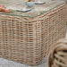 Corner detail of the Barakaldo Natural Antique Outdoor Seating Set's coffee table, highlighting the sturdy rattan weave and glass surface.