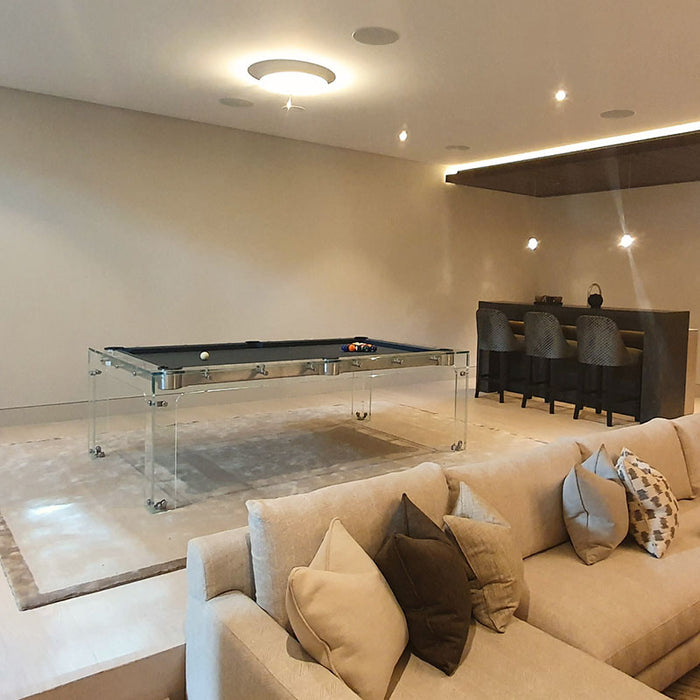 Elegant Carat Light transparent pool table with black felt in a luxurious entertainment lounge featuring a neutral palette and home bar.