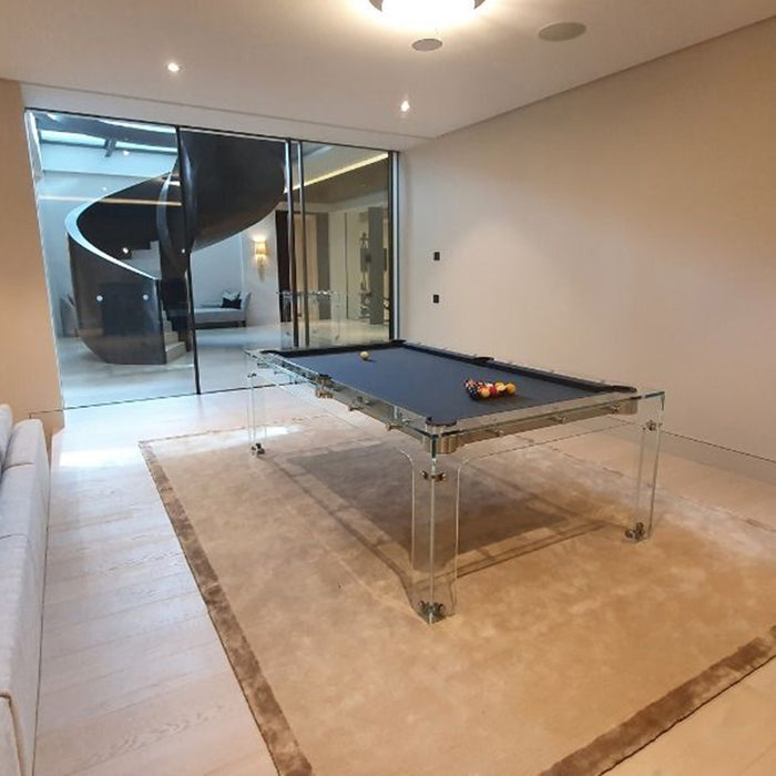 Transparent Carat Light pool table with navy felt, set on a plush beige rug in a sleek modern lounge with spiral staircase view.