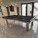 Black pool table in a glossy tiled interior with soft lighting and sliding glass doors opening to exterior.