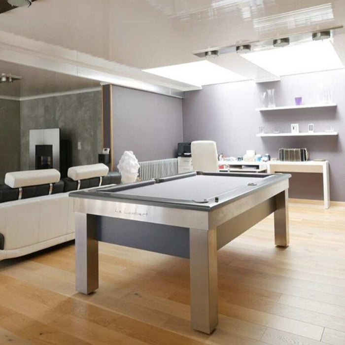 Stylish living room with the Billards Toulet Lambert Competition Pool Table featuring brushed metal legs and grey cloth, lit naturally under skylights.