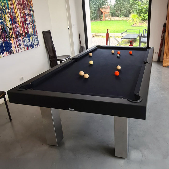 Black modern pool table with dark felt and chrome legs in a stylish room with garden views and contemporary art.