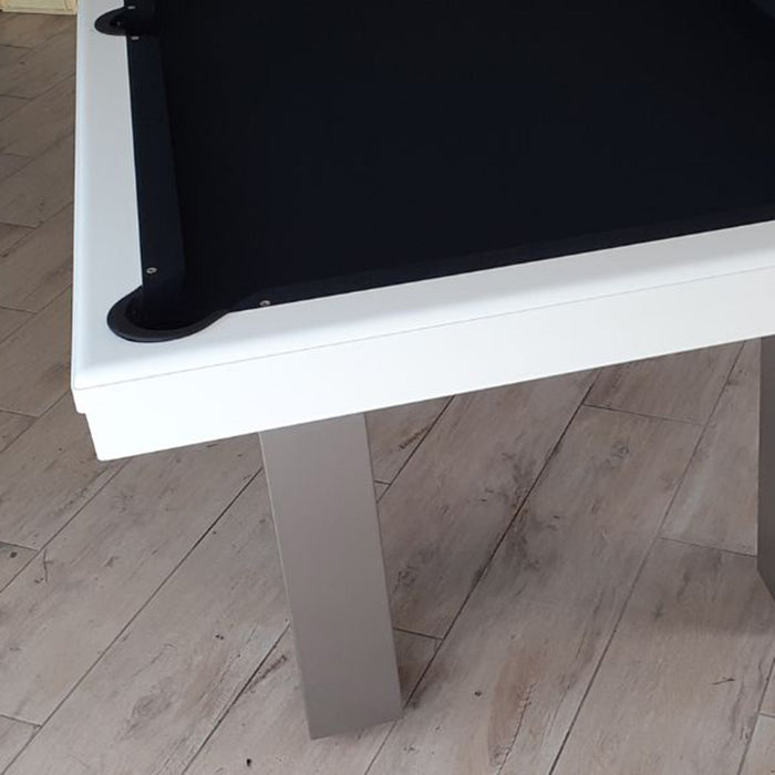 Modern white-framed pool table with black cloth, set in a bright room with wooden floors.