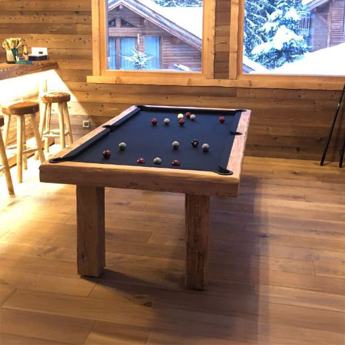 Warm timber games room with Billards Toulet Megeve pool table in black cloth and wooden legs, overlooking a snow-covered alpine view.