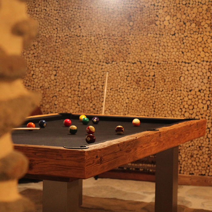 Warm-toned Billards Toulet Megeve Modern pool table with black felt in a stone-walled room featuring stacked wood decor and ambient lighting.