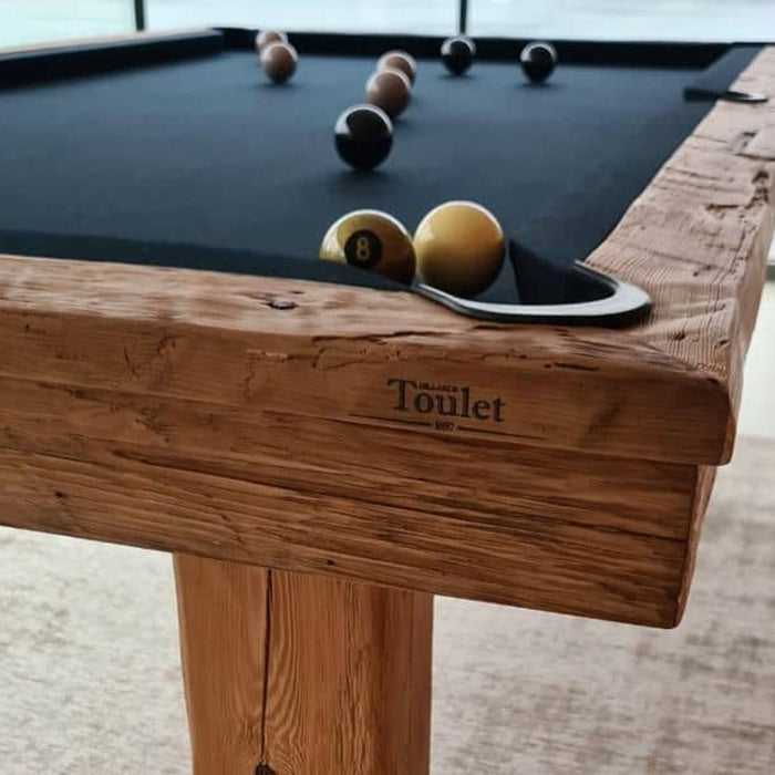 Close-up of Billards Toulet Megeve modern pool table with rustic solid wood frame, black cloth surface, and precision-cut pocket detail.