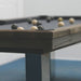 Close-up of Billards Toulet Megeve modern pool table featuring dark reclaimed wood edges, brushed metal legs, and black cloth in a minimalist games room.