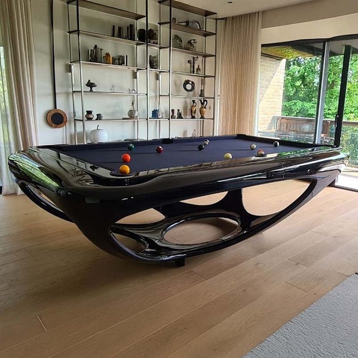 Glossy black Billards Toulet Whitelight pool table featured in a cosy, wood-floored room with a view of greenery and stylish shelf decor for a serene vibe.