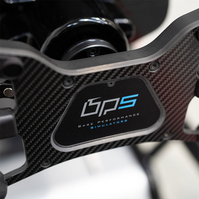 BPS Phoenix Commercial Racing Simulator carbon fibre steering wheel close-up showing BPS Base Performance Simulators logo badge with blue and white control buttons