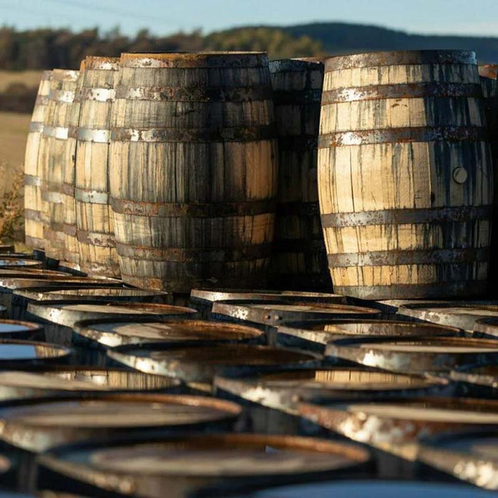 A collection of traditional whisky barrels in the scenic Speyside Valley, emphasising the heritage and authenticity of the materials.