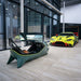 Curv AMR-C01-R Aston Martin Racing Simulator in the foreground with curved ultrawide monitor displaying Silverstone circuit, Aston Martin Racing No. 97 GTE car visible behind in the Aston Martin showroom