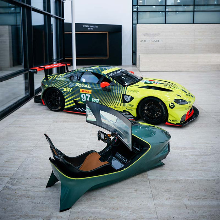 Curv AMR-C01-R Aston Martin Racing Simulator in British Racing Green and lime yellow, elevated view with the Aston Martin Racing No. 97 Total/Sky GTE car positioned behind in the Aston Martin facility