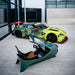Curv AMR-C01-R Aston Martin Racing Simulator in British Racing Green and lime yellow, elevated view with the Aston Martin Racing No. 97 Total/Sky GTE car positioned behind in the Aston Martin facility