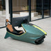 Curv AMR-C01-R Aston Martin Racing Simulator in British Racing Green and lime yellow, three-quarter front view showing brown leather interior seat and Samsung curved ultrawide monitor, photographed in the Aston Martin facility