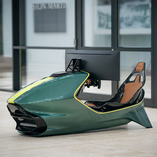 Curv AMR-C01-R Aston Martin Racing Simulator in British Racing Green with lime yellow trim, three-quarter passenger-side view showing the open cockpit with brown leather seat, photographed inside the Aston Martin Design Centre