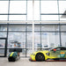 Curv AMR-C01-R Aston Martin Racing Simulator in matching green and yellow livery displayed beside the full-size Aston Martin Racing No. 97 GTE race car inside the Aston Martin facility