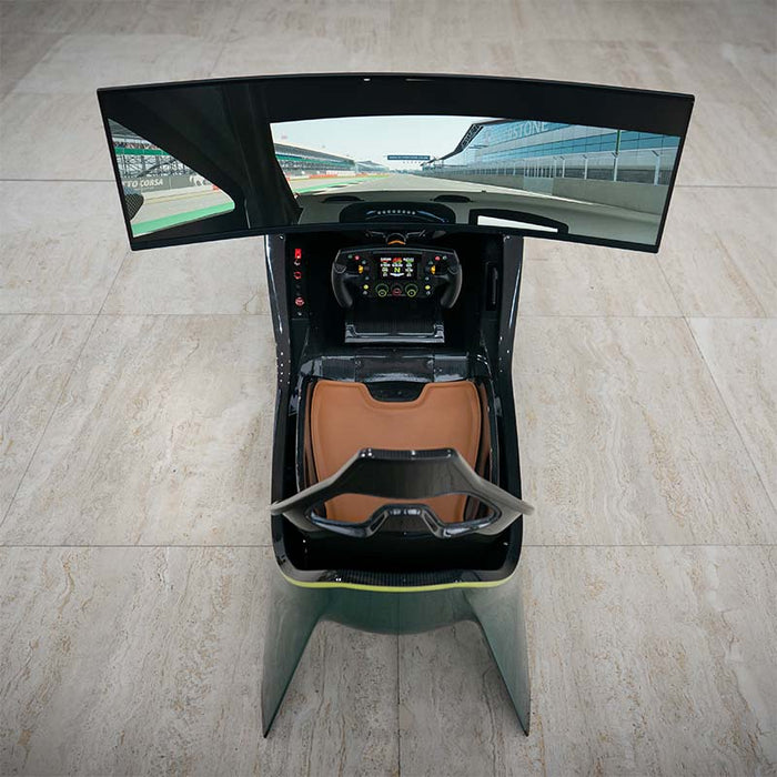 Curv AMR-C01-R Aston Martin Racing Simulator cockpit photographed from directly above showing brown leather racing seat, carbon fibre interior, Formula steering wheel with colour display, and curved triple-screen setup displaying Silverstone circuit