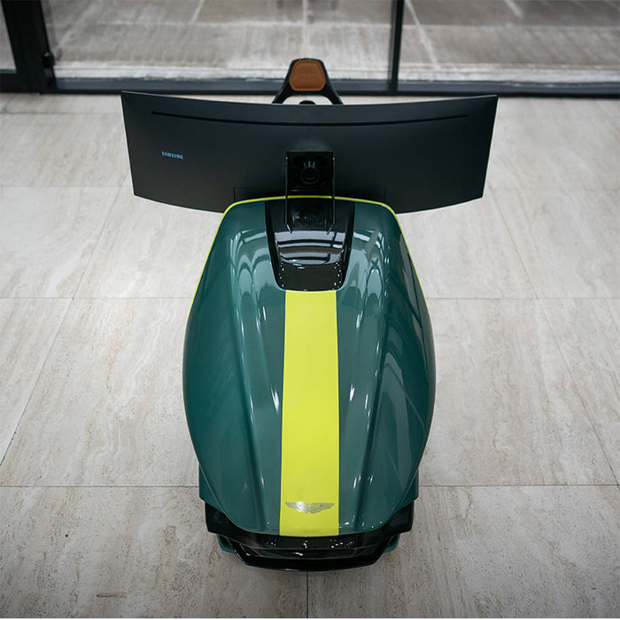 Curv AMR-C01-R Aston Martin Racing Simulator photographed from directly above showing British Racing Green bodywork with central lime yellow racing stripe and Aston Martin winged badge, Samsung curved ultrawide monitor visible at the top
