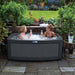 Women enjoying champagne and smiling in the DuoSpa S080 dark grey with grey panels in the garden. 