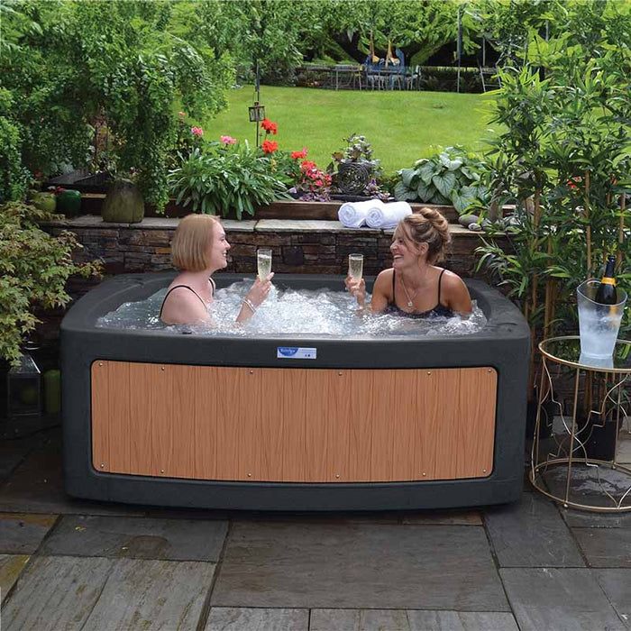 Women enjoying champagne and smiling in the DuoSpa S080 dark grey with teak panels in the garden. 