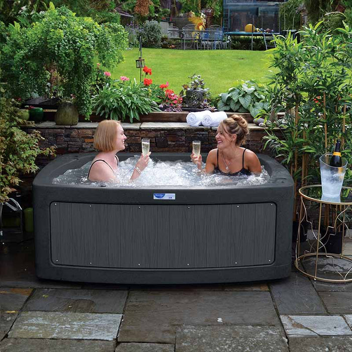 Two individuals unwinding in a DuoSpa S240 hot tub with wooden trim, outdoors.