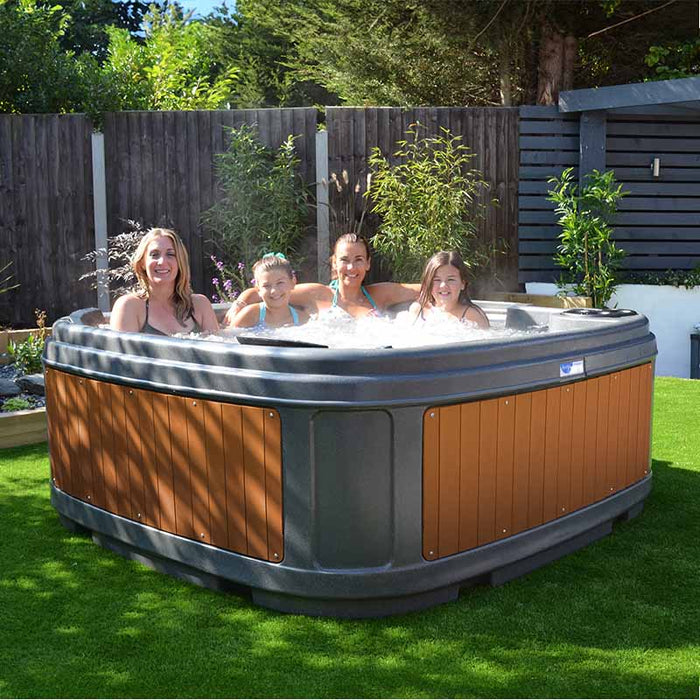 Family enjoying a sunny day in a dark grey hot tub in a green garden.