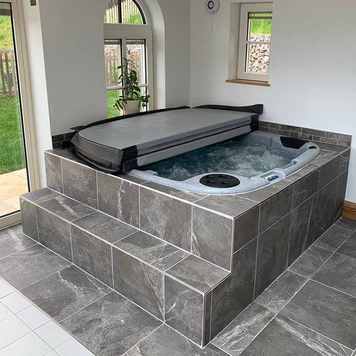 Grey hot tub with wooden panels, seamlessly integrated into a stone patio setting.