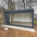 Dark-painted Estholz Garden House WILLIAM with a full-length glass wall, positioned in a quiet, leafless garden landscape.