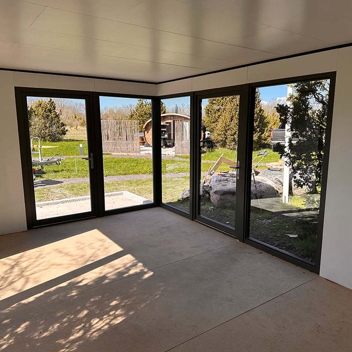 Spacious corner interior of Estholz Garden House WILLIAM featuring full-height glass doors allowing ample natural light and outdoor visibility.