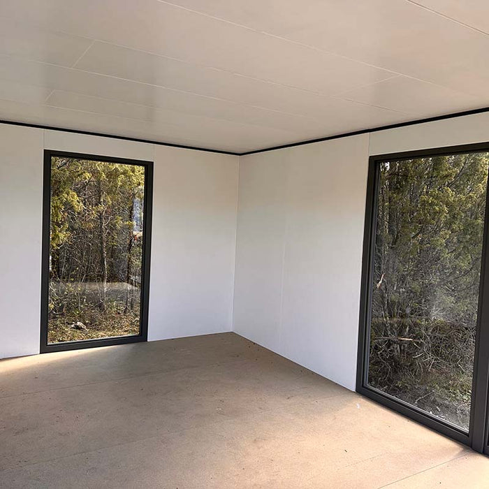 Unfurnished interior of Estholz Garden House WILLIAM showcasing white walls and large black-framed windows with forest views.
