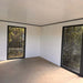 Unfurnished interior of Estholz Garden House WILLIAM showcasing white walls and large black-framed windows with forest views.