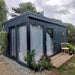 Modern Estholz Summerhouse WALTER with dark timber cladding, large glass windows, and minimal patio seating surrounded by greenery – perfect for garden retreats or home offices.
