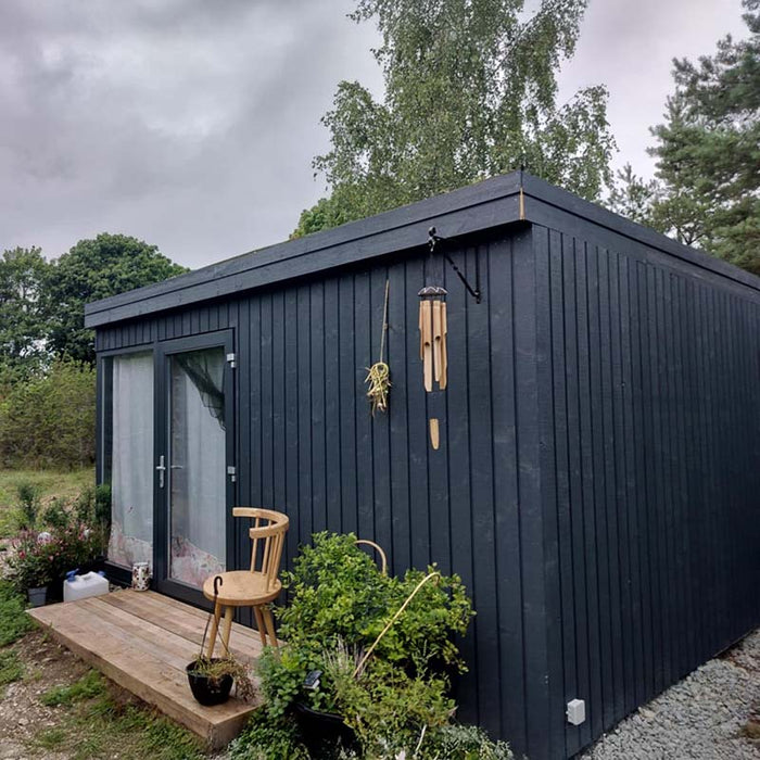 Full side view of Estholz Summerhouse WALTER showcasing its sleek dark wood exterior, minimalist design, and tranquil natural surroundings ideal for outdoor living.