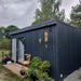 Full side view of Estholz Summerhouse WALTER showcasing its sleek dark wood exterior, minimalist design, and tranquil natural surroundings ideal for outdoor living.