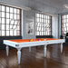Etrusco Smile pool table in a white finish with vibrant orange cloth, featured in an industrial-style loft with large grid windows.