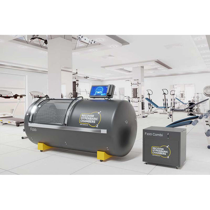 Angled view of F100 steel hyperbaric chamber with equipment in gym setting.