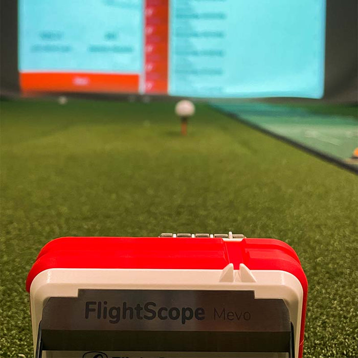 FlightScope Mevo aiming at a golf simulation screen, shallow depth of field.